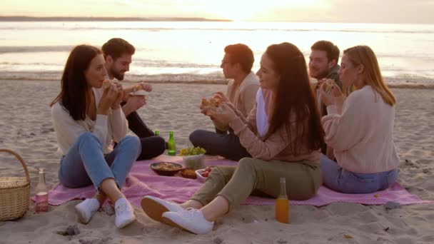 Amigos felices comiendo sándwiches en el picnic en la playa — Vídeo de stock