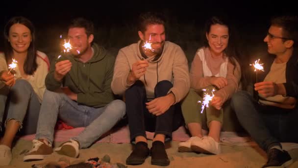 Amigos felizes com faíscas no fogo do acampamento à noite — Vídeo de Stock