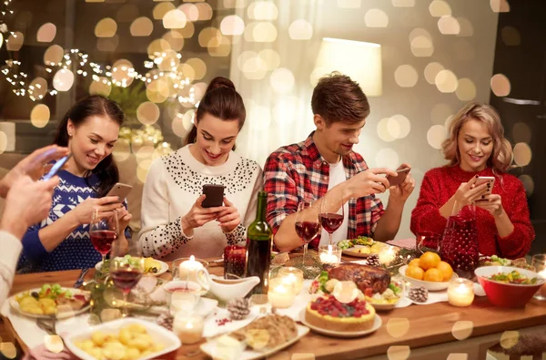 Friends with smartphones having christmas dinner — Stock Photo, Image