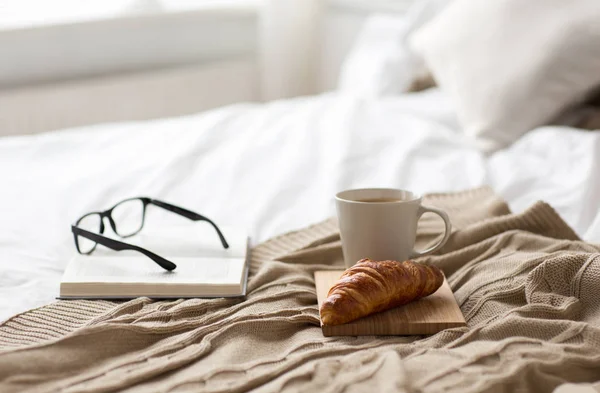 Kaffee, Croissant, Decke und Buch auf dem heimischen Bett — Stockfoto