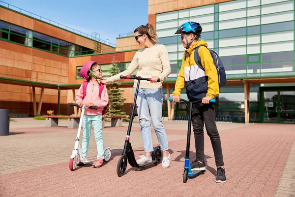 Szczęśliwy szkoła dzieci z matka jazdy skutery — Zdjęcie stockowe