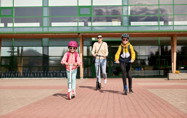 Niños de la escuela feliz con la madre que monta scooters —  Fotos de Stock