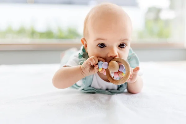 baby girl on white blanket chewing wooden rattle