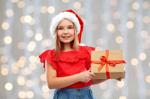 Uśmiechnięta dziewczyna w kapeluszu Mikołaja z prezentem świątecznym — Zdjęcie stockowe