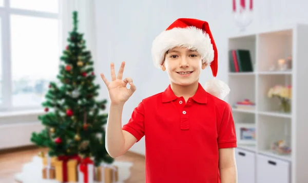 微笑的男孩在圣诞老人帮手帽子显示OK手势 — 图库照片
