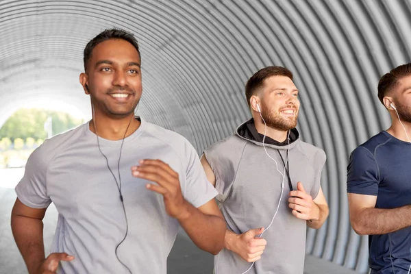 Male friends with earphones running outdoors — Stock Photo, Image