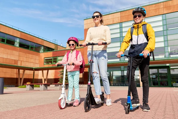 Heureux écoliers avec mère équitation scooters — Photo