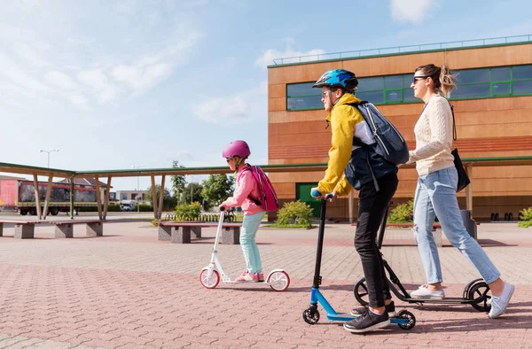 Niños de la escuela feliz con la madre que monta scooters —  Fotos de Stock