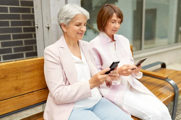 Счастливые пожилые женщины со смартфонами в городе — стоковое фото