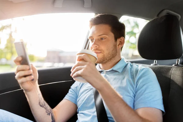 Passagerare dricker kaffe med smartphone i bilen — Stockfoto