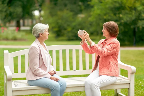 Senior woman photographing her friend at park — Stock Photo, Image