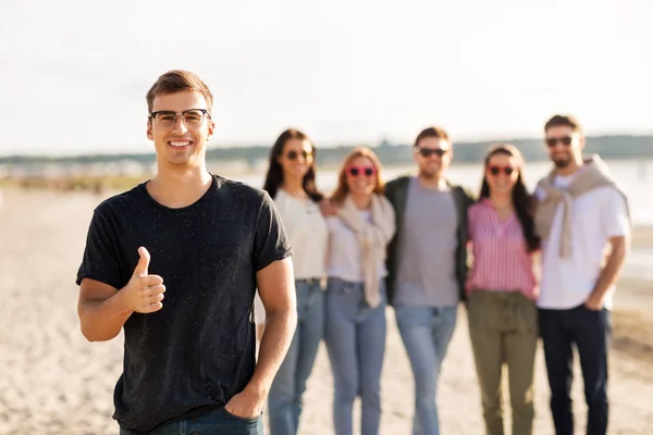 Glad man med vänner på stranden visar tummen upp — Stockfoto