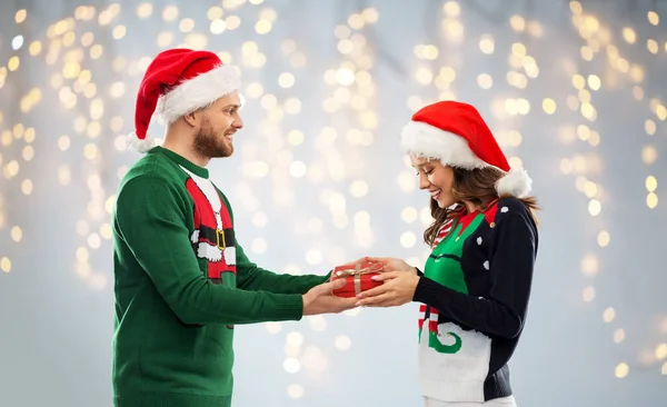 Casal feliz em camisolas feias com presente de Natal — Fotografia de Stock