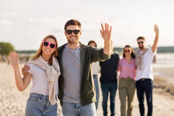 Couple heureux avec des amis agitant les mains sur la plage — Photo