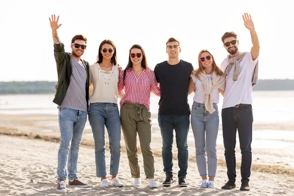 Glada vänner viftar med händerna på stranden på sommaren — Stockfoto
