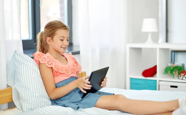 Smiling girl with tablet pc sitting on bed at home — Stock Photo, Image