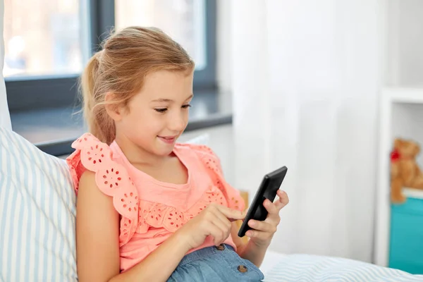 Girl using smartphone sitting on bed at home — Stock Photo, Image