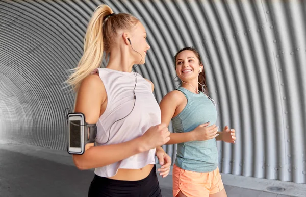 Mujeres jóvenes con auriculares y smartphones funcionando — Foto de Stock