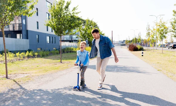 Gelukkig vader en zoontje paardrijden scooter in stad — Stockfoto