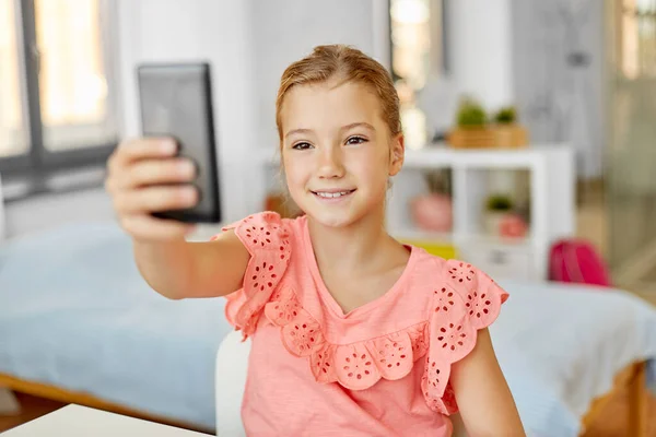 Menina feliz com smartphone levando selfie em casa — Fotografia de Stock