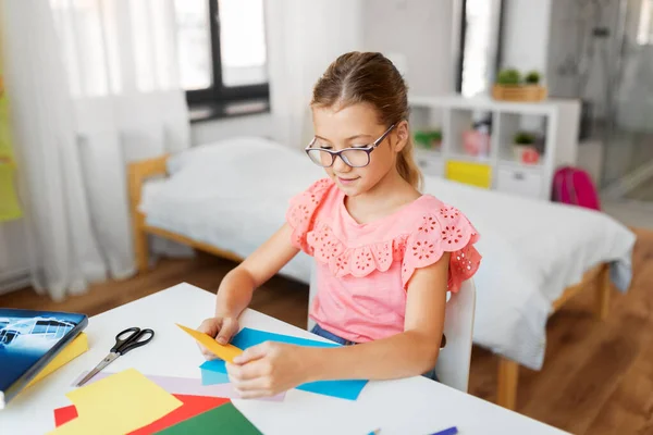 Flicka med färg papper sitter på bordet hemma — Stockfoto