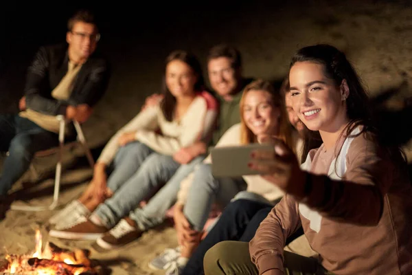 Amigos felices tomando selfie en el fuego del campamento en la playa — Foto de Stock