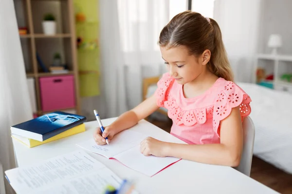 Estudante menina com livro escrevendo para notebook em casa — Fotografia de Stock