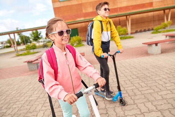 Gelukkige schoolkinderen met rugzakken en scooters — Stockfoto