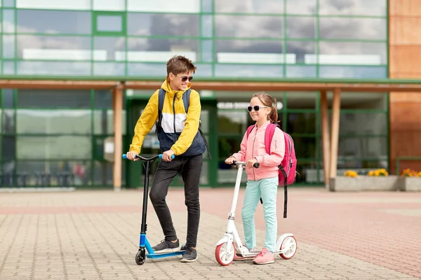 Gelukkige schoolkinderen met rugzakken en scooters — Stockfoto