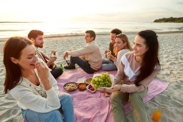 Happy friends eating sandwiches at picnic on beach — Stock Photo, Image