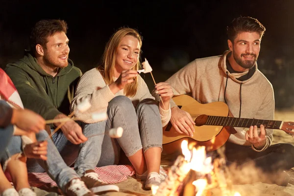 Amigos tostando malvavisco y tocando la guitarra — Foto de Stock