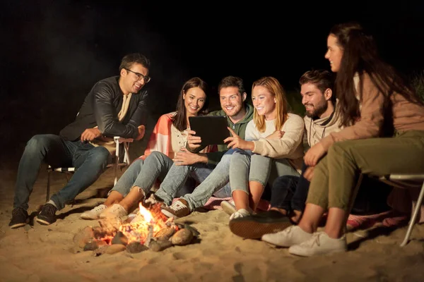 Vrienden met tablet pc in brand op het strand 's nachts — Stockfoto