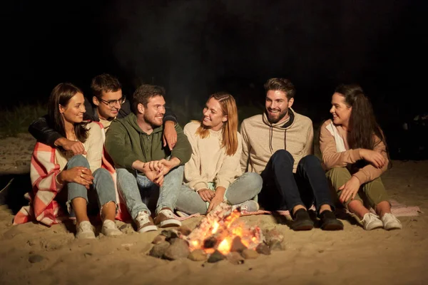 Groep vrienden zittend op kampvuur op het strand — Stockfoto