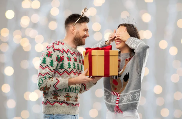 Счастливая пара в уродливых свитерах с рождественским подарком — стоковое фото