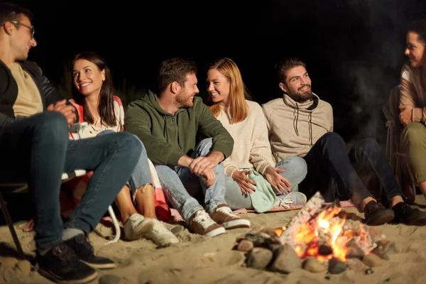 Groep vrienden zittend op kampvuur op het strand — Stockfoto