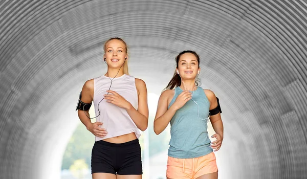 イヤホンやスマートフォンを持つ若い女性が走っている — ストック写真