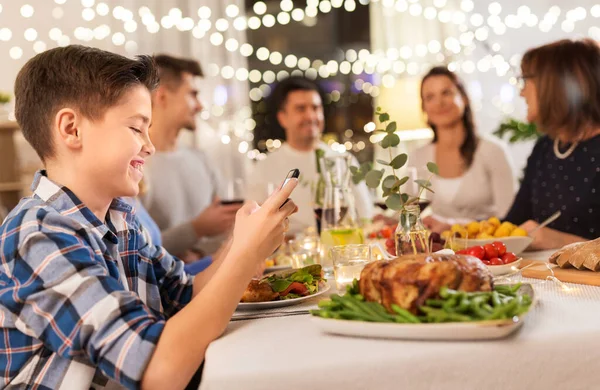 Chłopiec ze smartfonem na rodzinnej kolacji — Zdjęcie stockowe