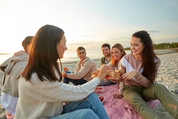 Glada vänner äter smörgåsar på picknick på stranden — Stockfoto