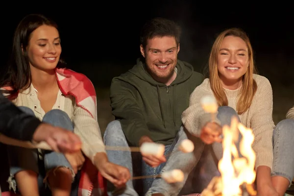 Amigos tostando malvavisco en fuego de campamento por la noche — Foto de Stock