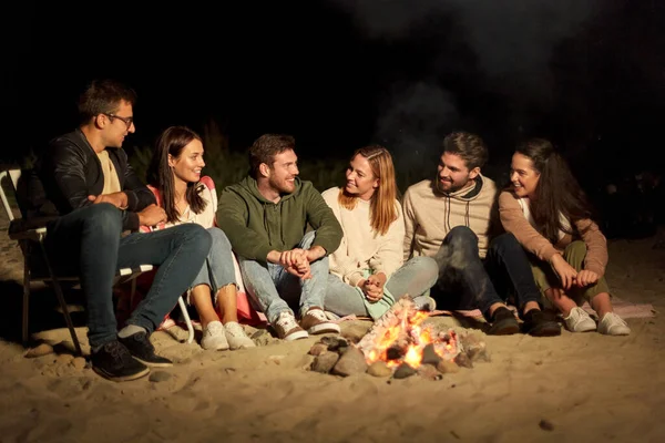 Groep vrienden zittend op kampvuur op het strand — Stockfoto