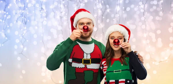 Happy couple in christmas sweaters and santa hats — Stock Photo, Image