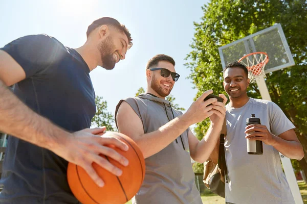 Мужчины со смартфоном на баскетбольной площадке — стоковое фото