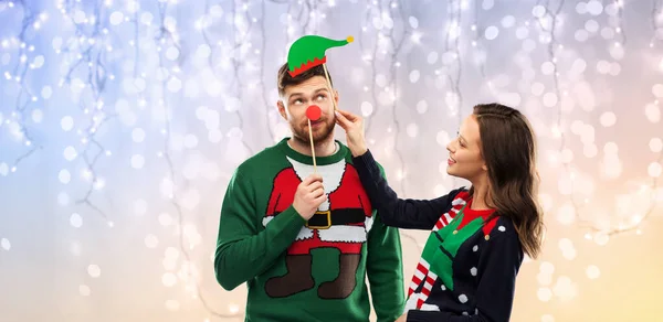 Пара с рождественским реквизитом в уродливых свитерах — стоковое фото