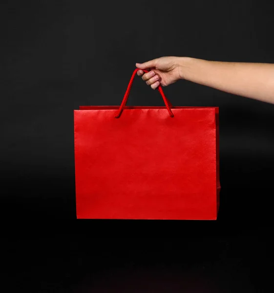 Mano sosteniendo bolsa de compras roja sobre fondo negro — Foto de Stock