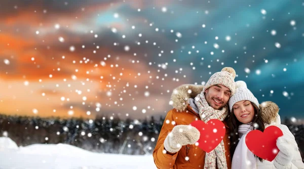 Happy couple with red hearts over winter landscape — Stock Photo, Image