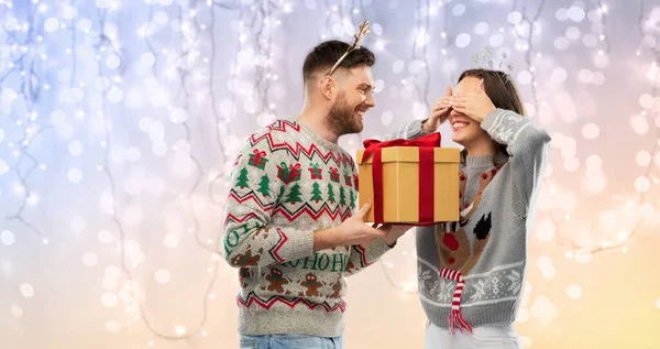 Casal feliz em camisolas feias com presente de Natal — Fotografia de Stock