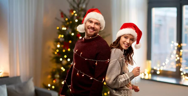 Para w kapeluszach Mikołaja związane przez girlandy Bożego Narodzenia — Zdjęcie stockowe