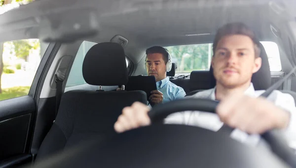 Uomo con tablet pc e cuffie guida in auto — Foto Stock