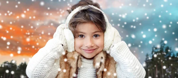 Glückliches kleines Mädchen mit Ohrenschützern über dem Winterwald — Stockfoto