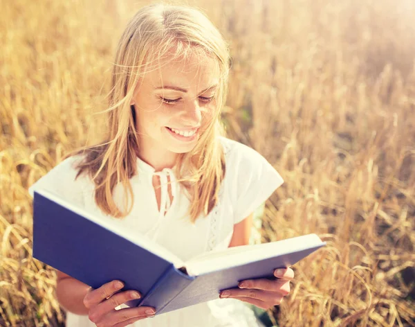 Uśmiechnięta młoda kobieta czytanie książki na polu zbóż — Zdjęcie stockowe